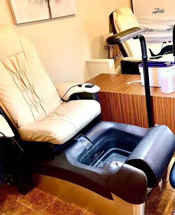 A beige pedicure spa chair with a built-in footbath, next to a small wooden table, in a salon setting. Copperfalls Aveda Spa & Salon, Castle Rock, CO