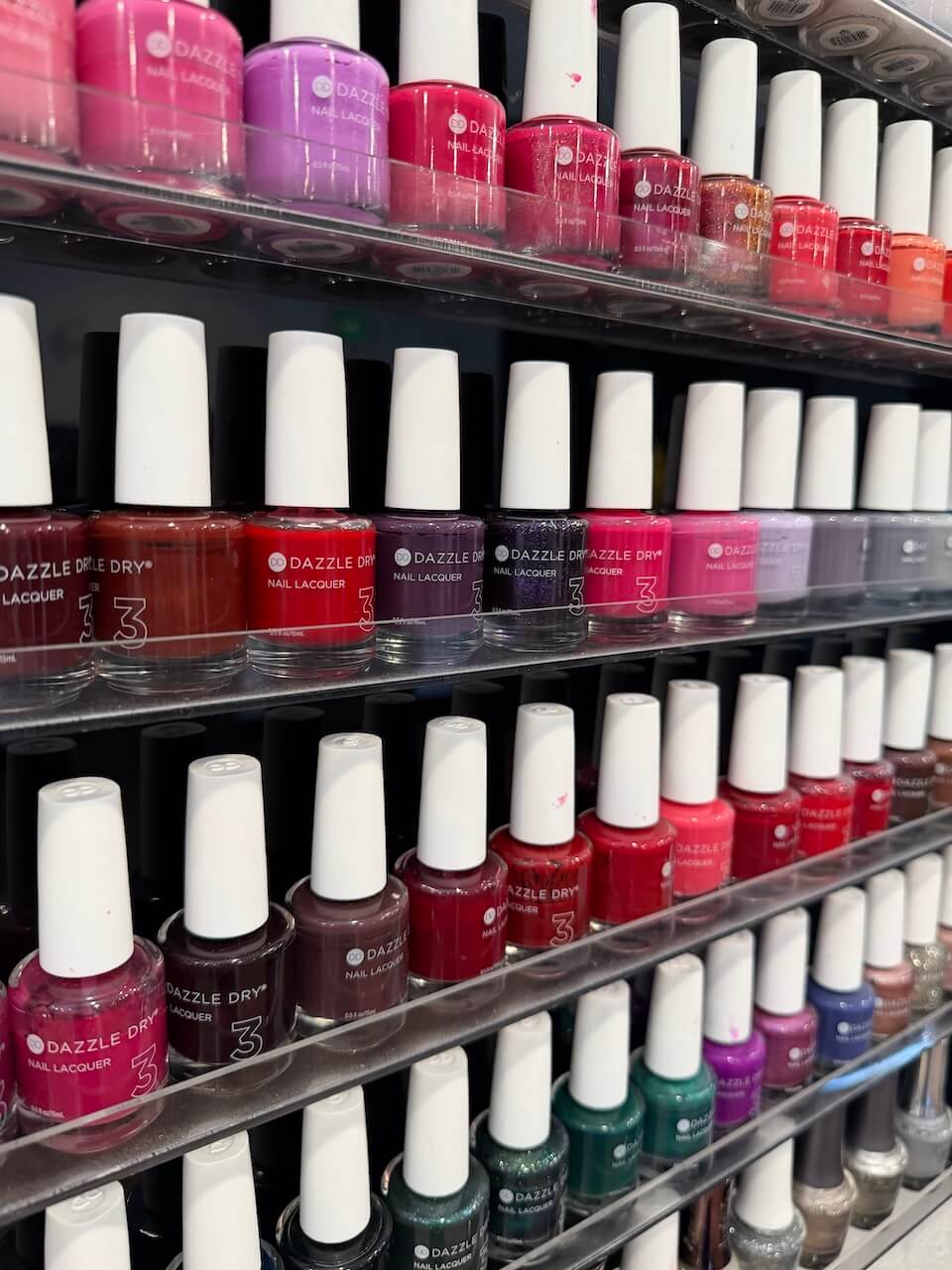 Shelves display rows of Dazzle Dry nail polish bottles in various colors, including shades of red, pink, purple, green, and brown. Copperfalls Aveda Spa & Salon, Castle Rock, CO