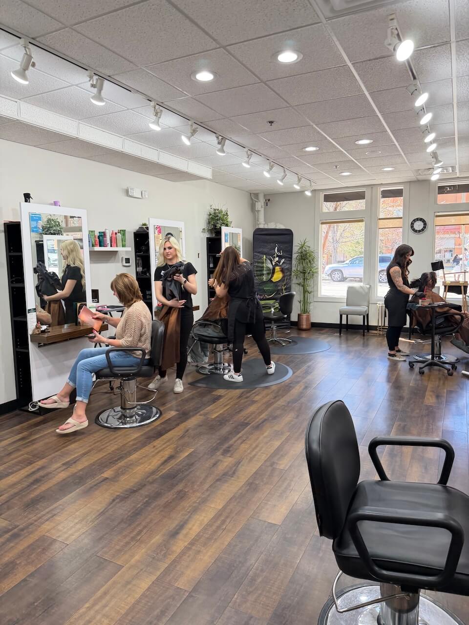 Four hairstylists work with clients in a bright, modern salon with wooden floors and large windows. Copperfalls Aveda Spa & Salon, Castle Rock, CO